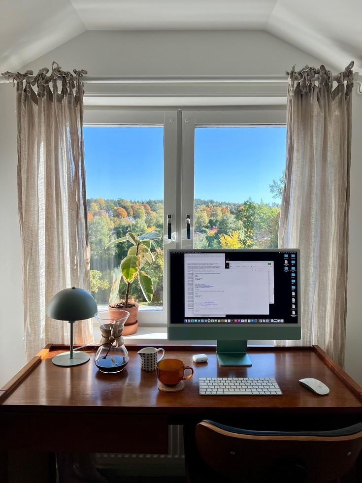 a desktop computer sitting on top of a wooden desk in front of a large window