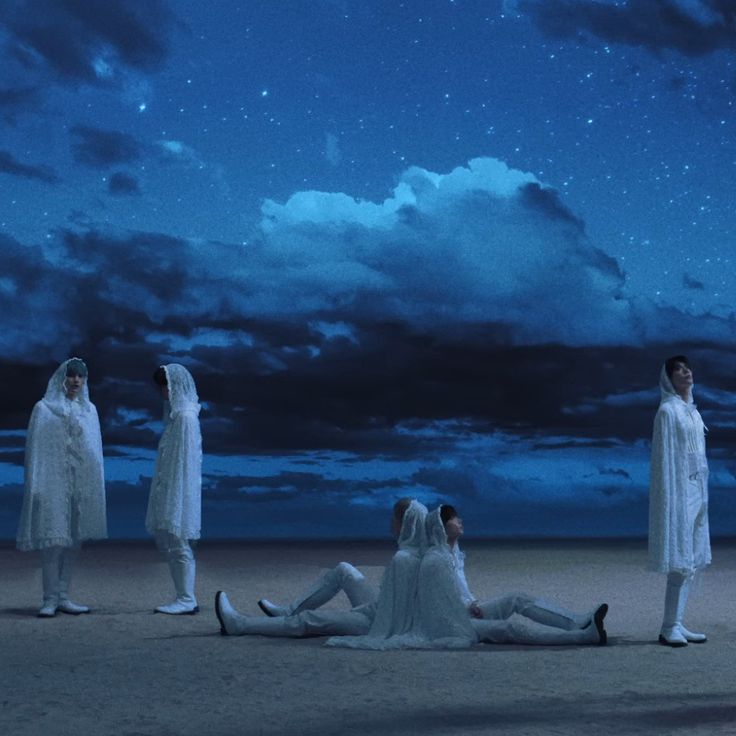 four people dressed in white sitting on the ground under a sky filled with stars and clouds