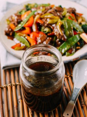 a glass jar filled with food sitting on top of a bamboo mat next to a plate of vegetables