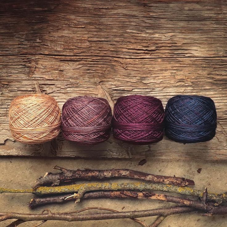 three balls of yarn sitting on top of a wooden floor next to sticks and twigs