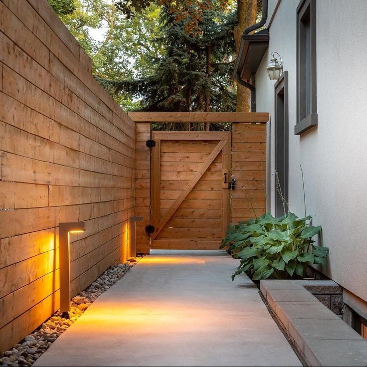 a wooden fence with lights on the side of it next to a building and trees