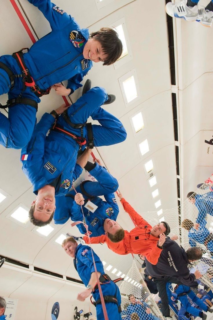 two men in blue jumpsuits are suspended from the ceiling while others look on