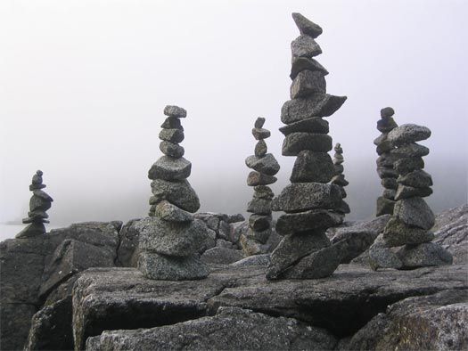 stacks of rocks sitting on top of a rocky hillside next to the ocean with fog in the background