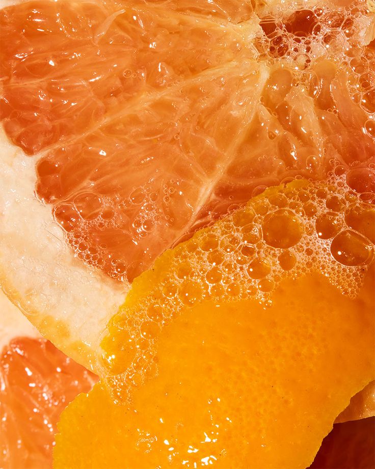 an orange sliced in half with water droplets on it's side and another piece of fruit next to it