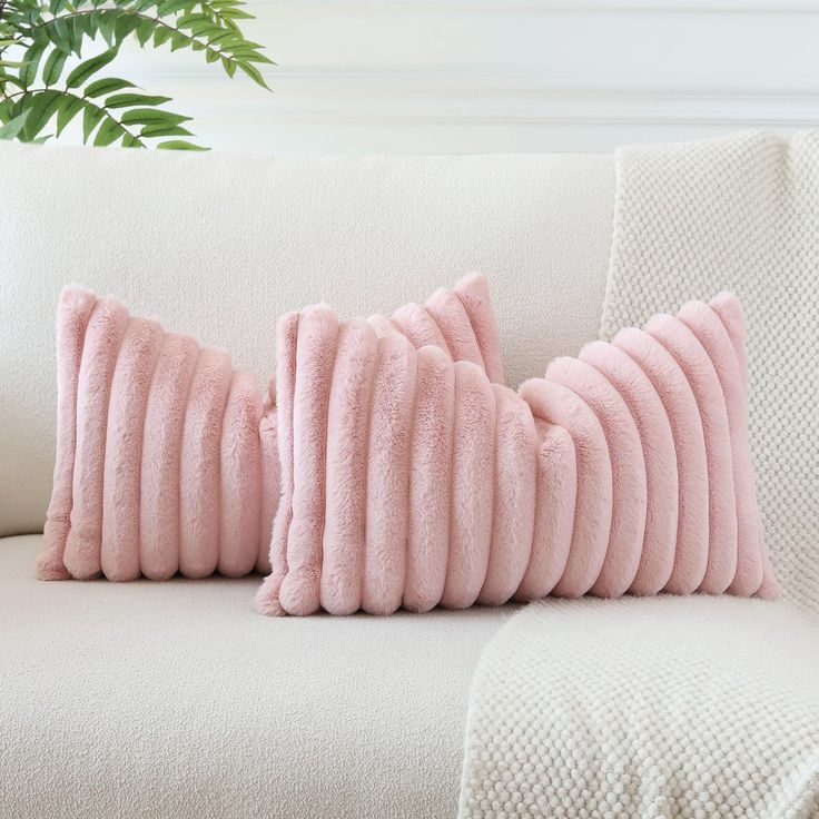 two pink pillows sitting on top of a white couch next to a potted plant