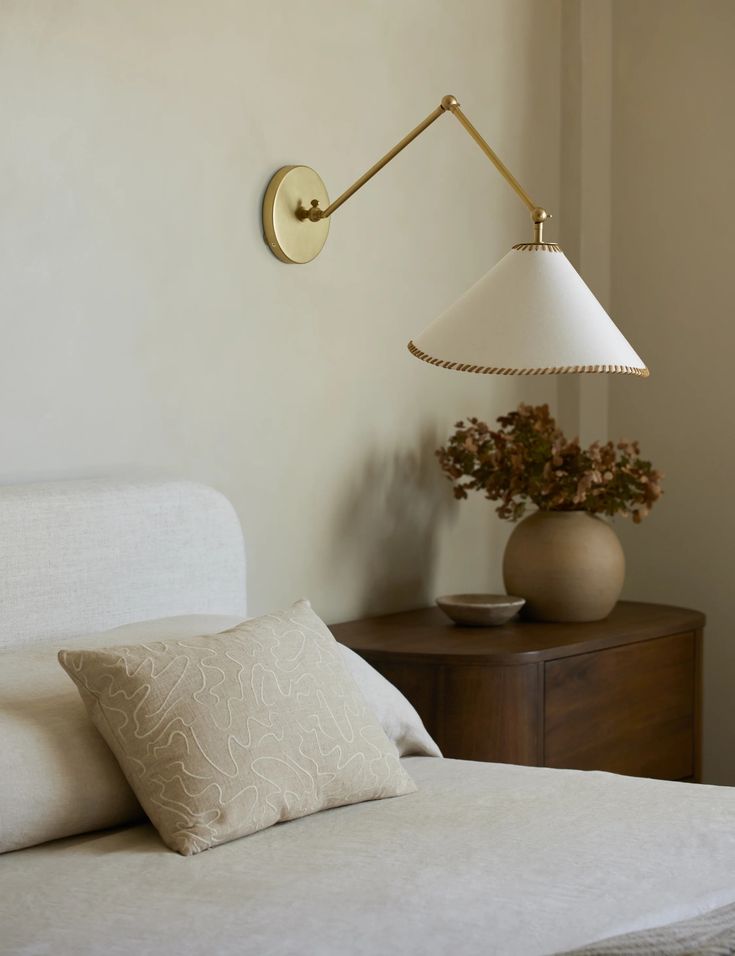 a white bed sitting next to a lamp on a wall