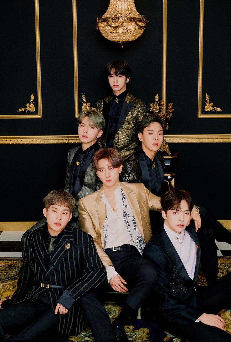 group of young men in suits sitting on a couch with gold chandelier behind them