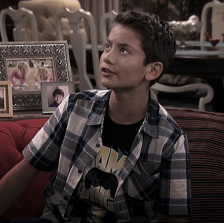 a young man sitting on top of a red couch next to a table with pictures