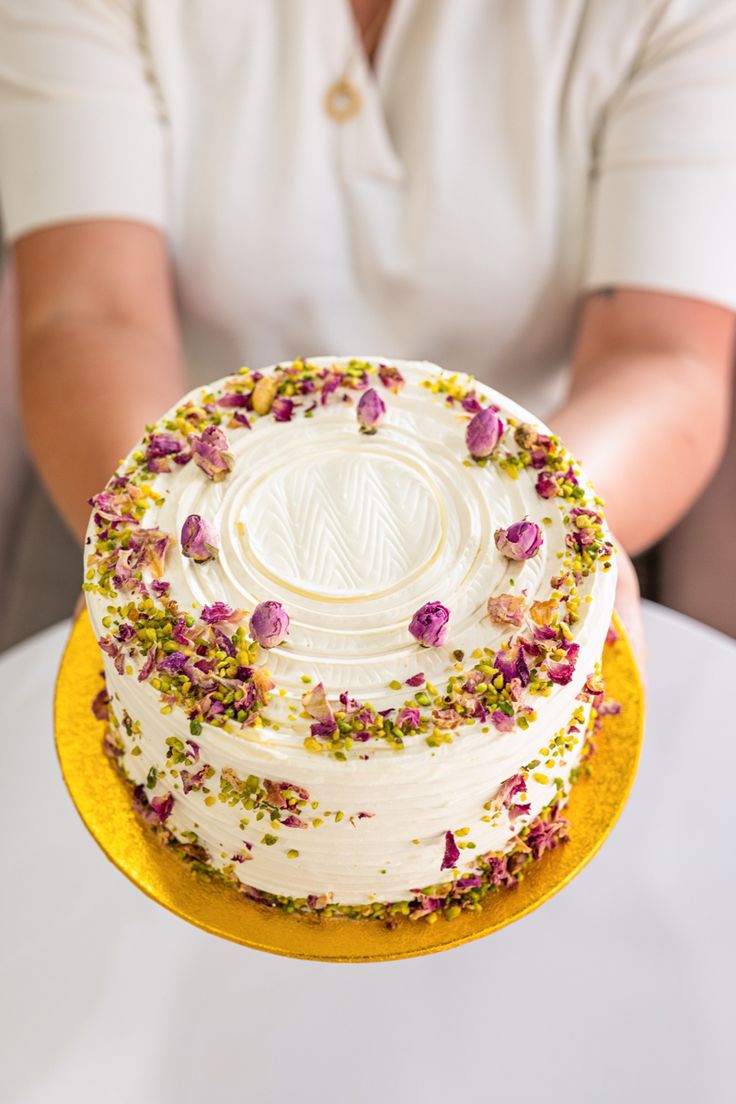 a person holding a cake with flowers on it