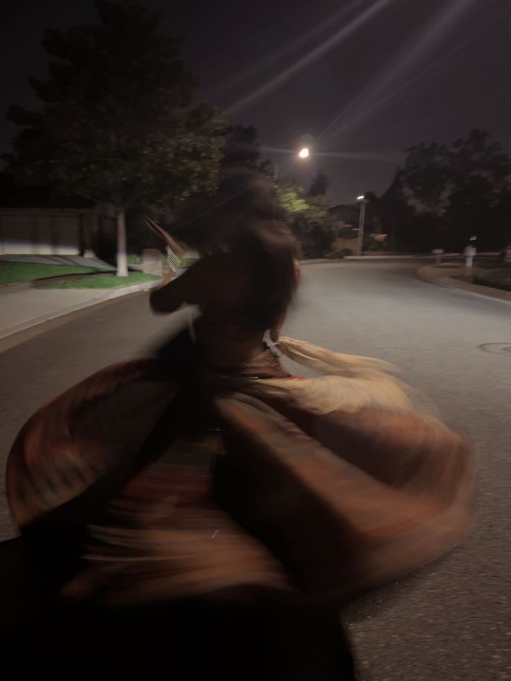 a woman is walking down the street at night with her dress blowing in the wind