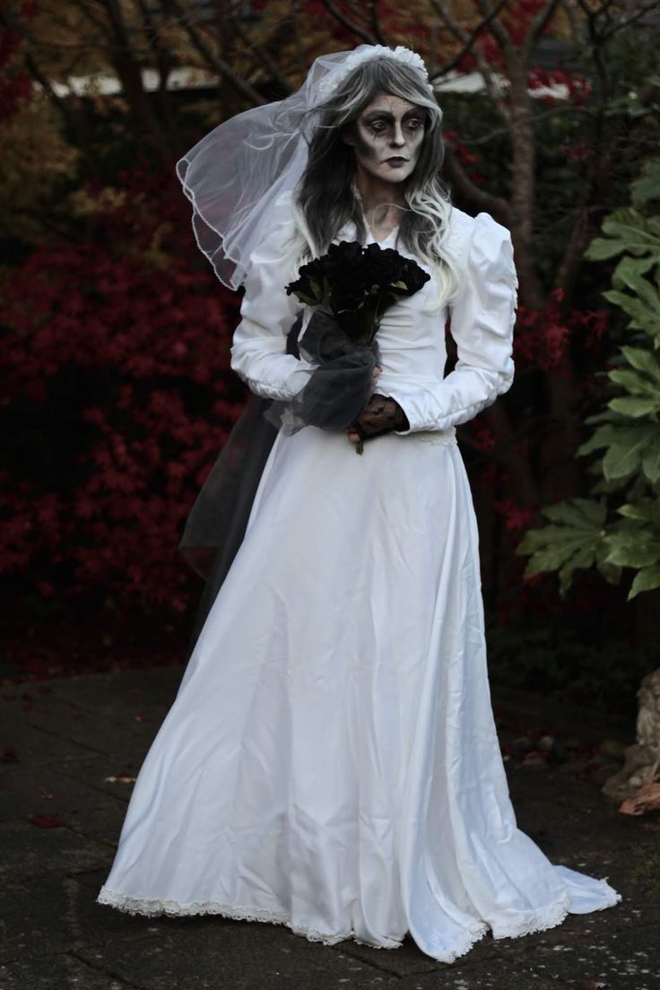 a woman dressed in white is holding a black teddy bear and wearing a wedding dress