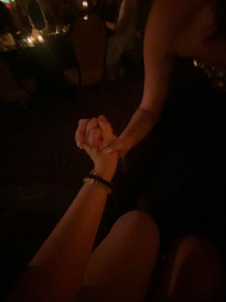 two people holding hands in the dark with lights on and one person wearing a black shirt