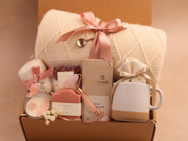 an open box with various items in it and a pink ribbon on the top, sitting on a table