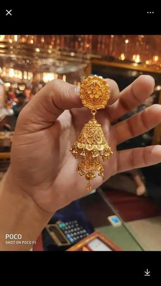 a person holding up a pair of gold earrings