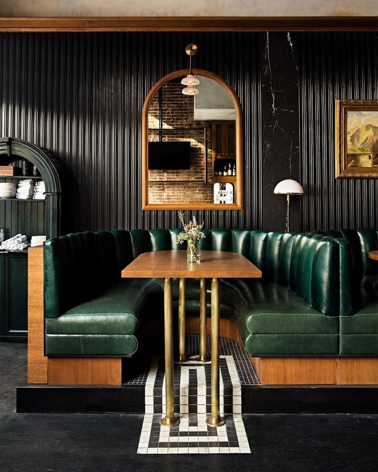 a green leather couch sitting next to a wooden table in front of a black wall