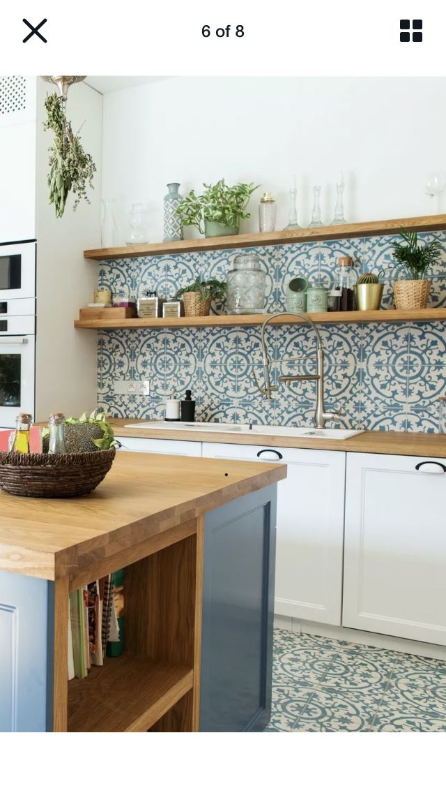 a kitchen with blue and white tiles on the wall, shelves above an island counter