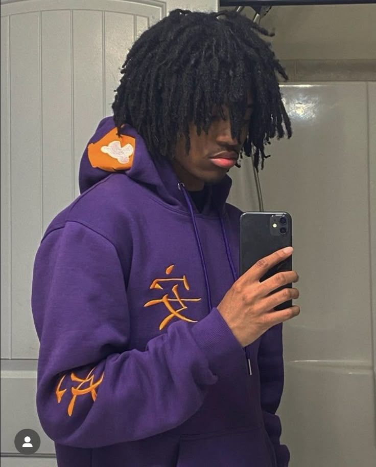 a man with dreadlocks is looking at his cell phone while wearing a purple hoodie