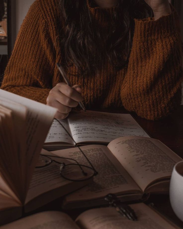 a woman sitting at a table in front of an open book and holding a pen