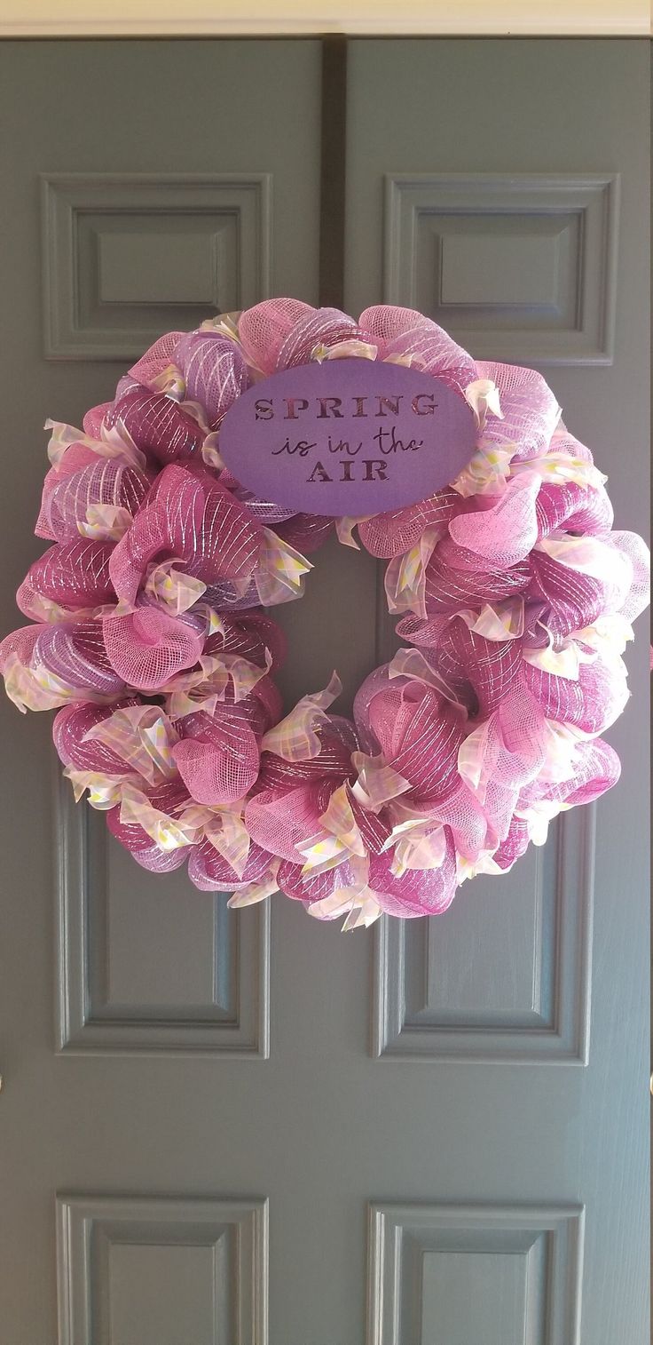 a purple wreath with pink flowers on it is hanging from the front door to welcome visitors