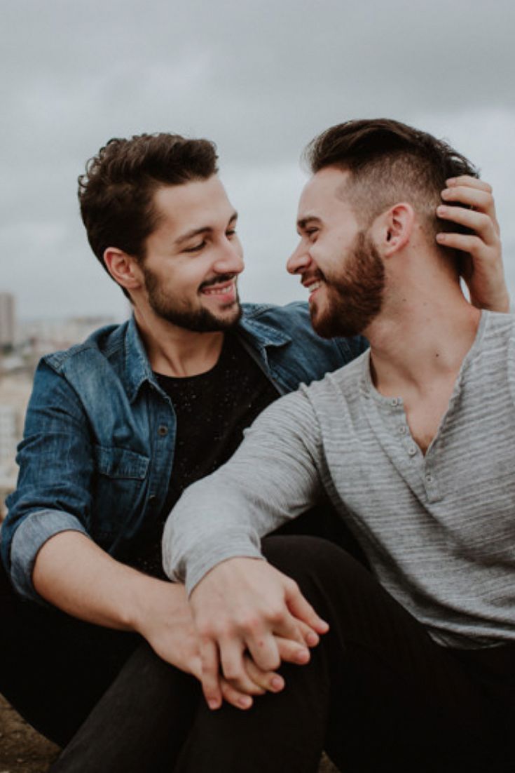 two men sitting next to each other on top of a cement wall looking at each other