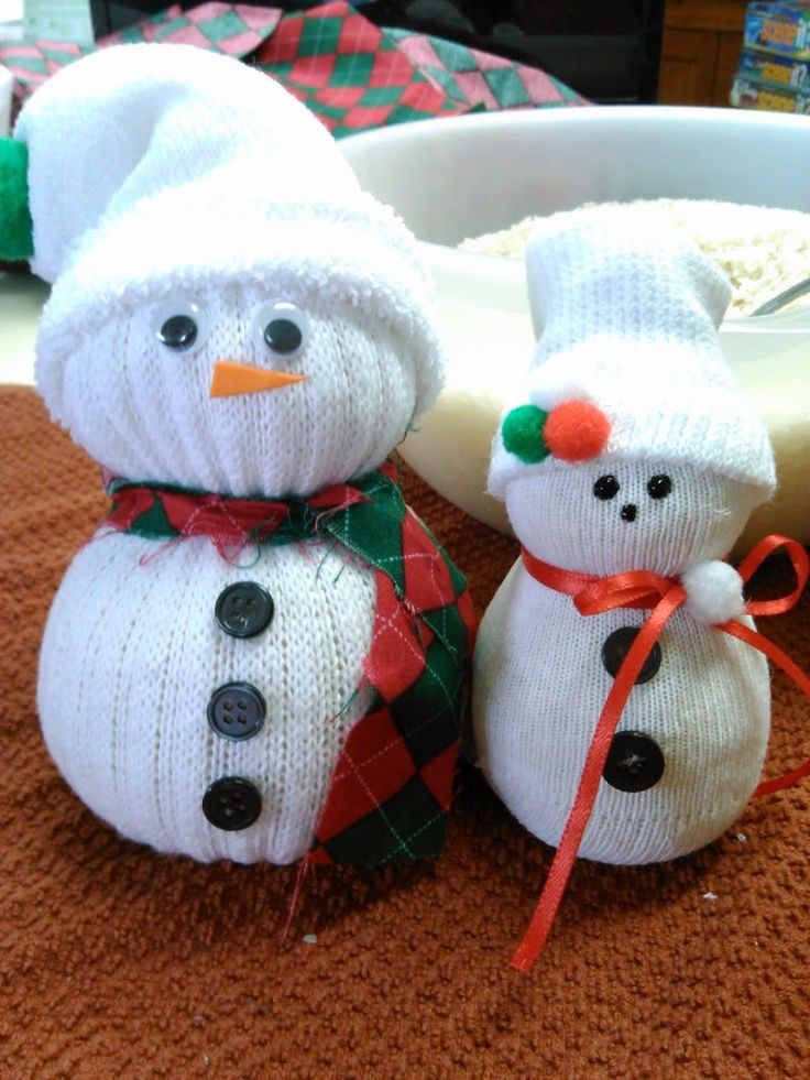 two knitted snowmen sitting next to each other on top of a brown table