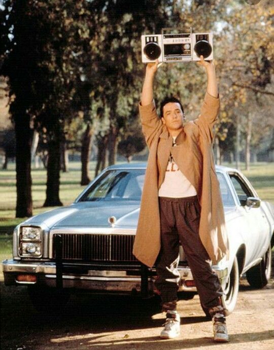 a man holding up a radio above his head in front of a car