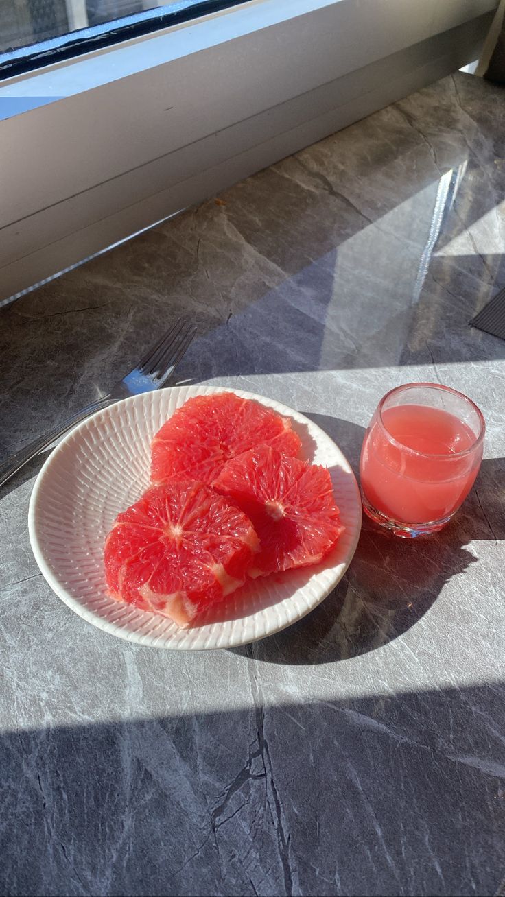 grapefruit slices on a plate next to a glass of watermelon juice