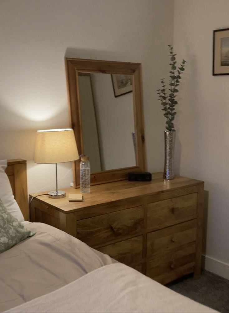 a wooden dresser sitting next to a bed with a lamp and mirror on top of it