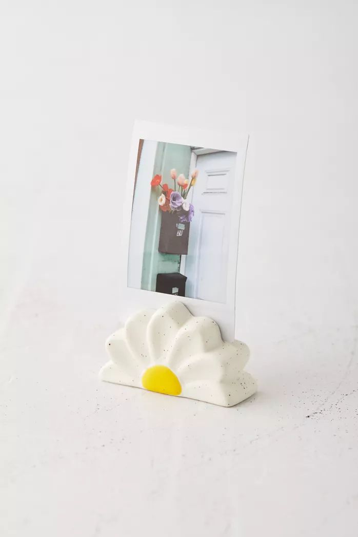 a white photo frame sitting on top of a table next to a vase with flowers in it