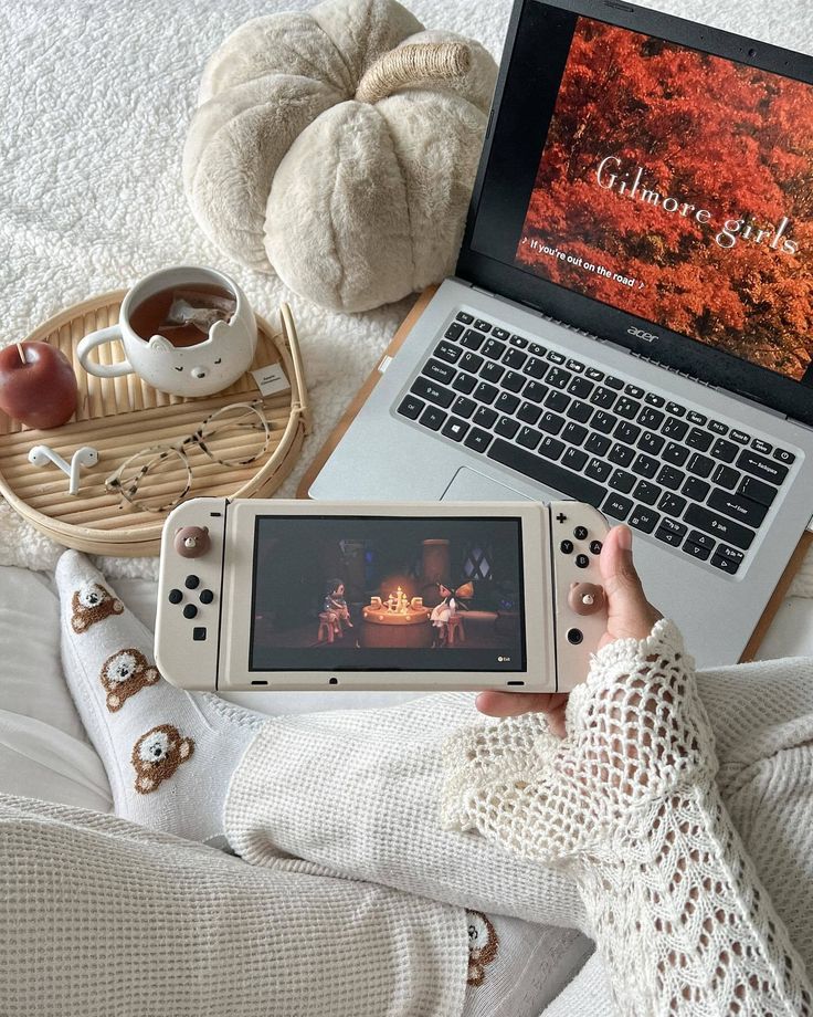 a person holding a nintendo wii game controller in front of a laptop on a bed