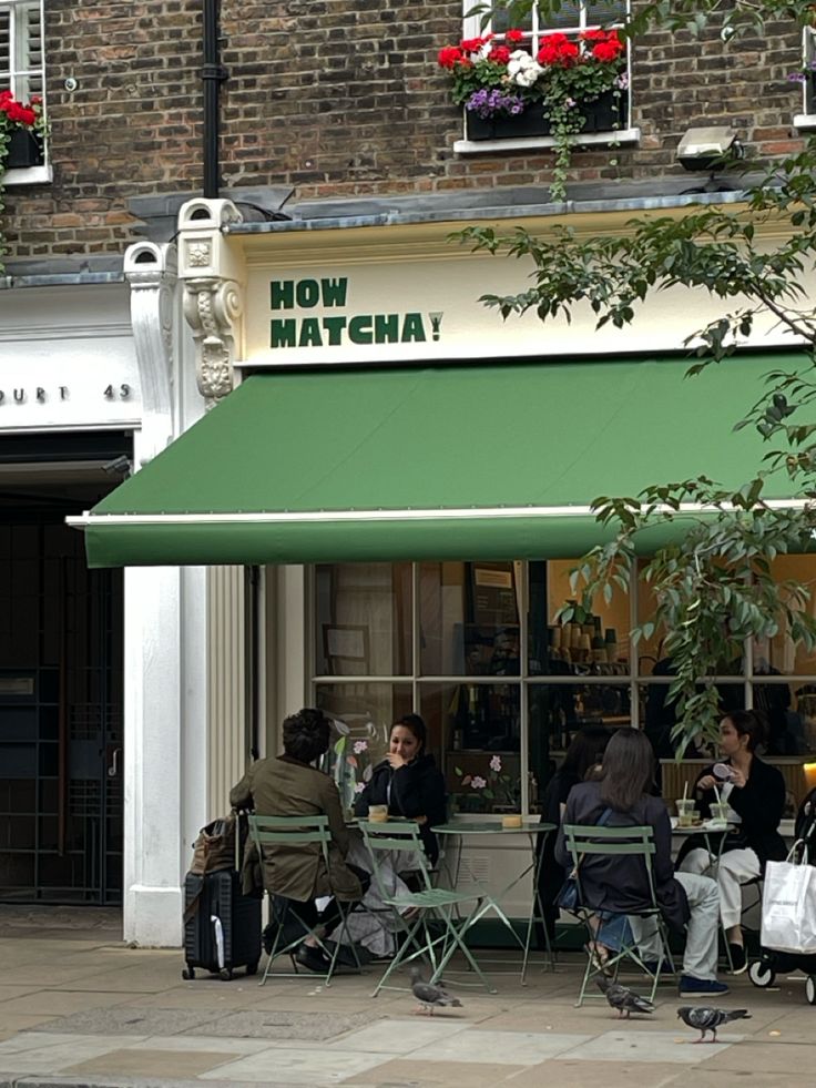 people sitting at tables in front of a store with green awnings and flowers