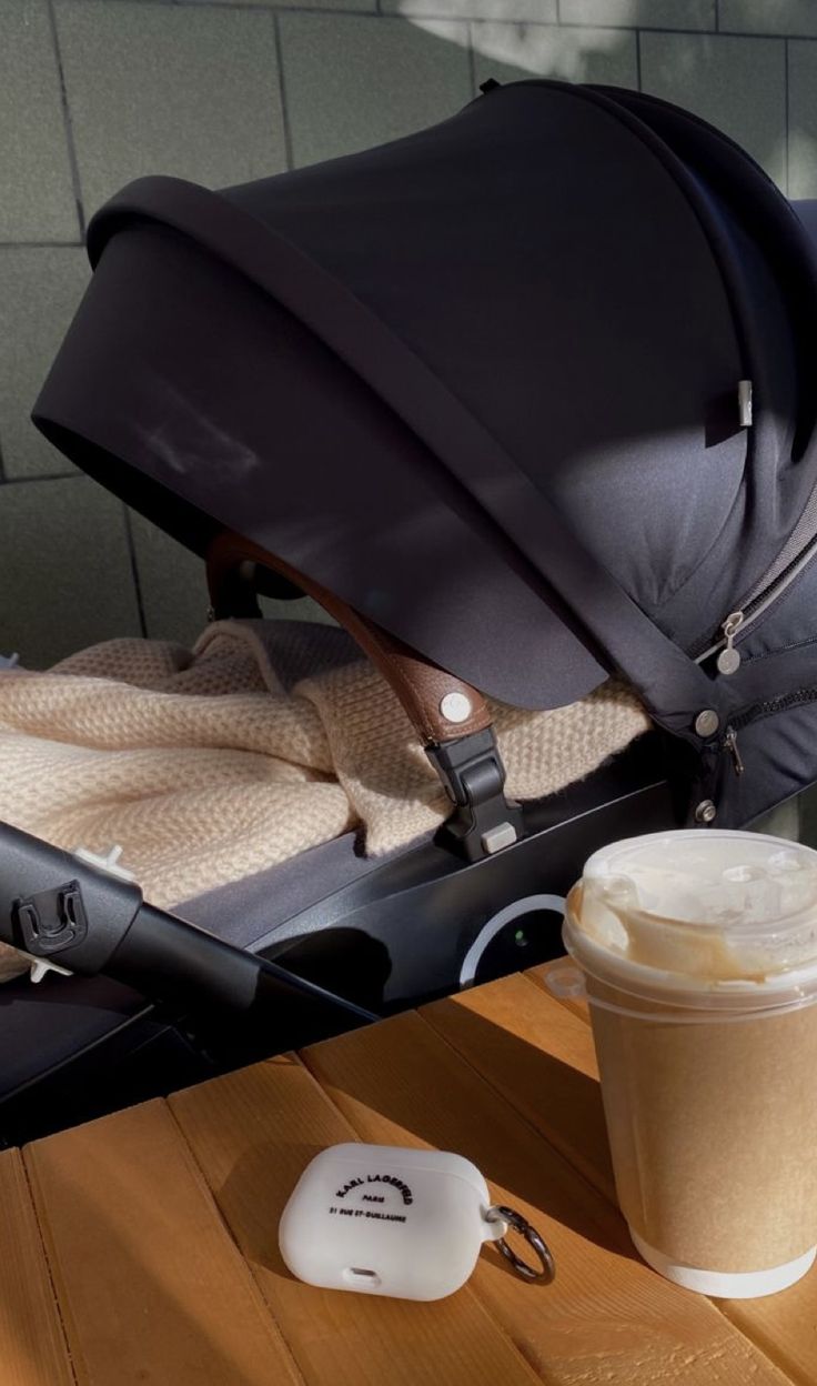 a cup of coffee sitting next to a stroller with a blanket on the seat