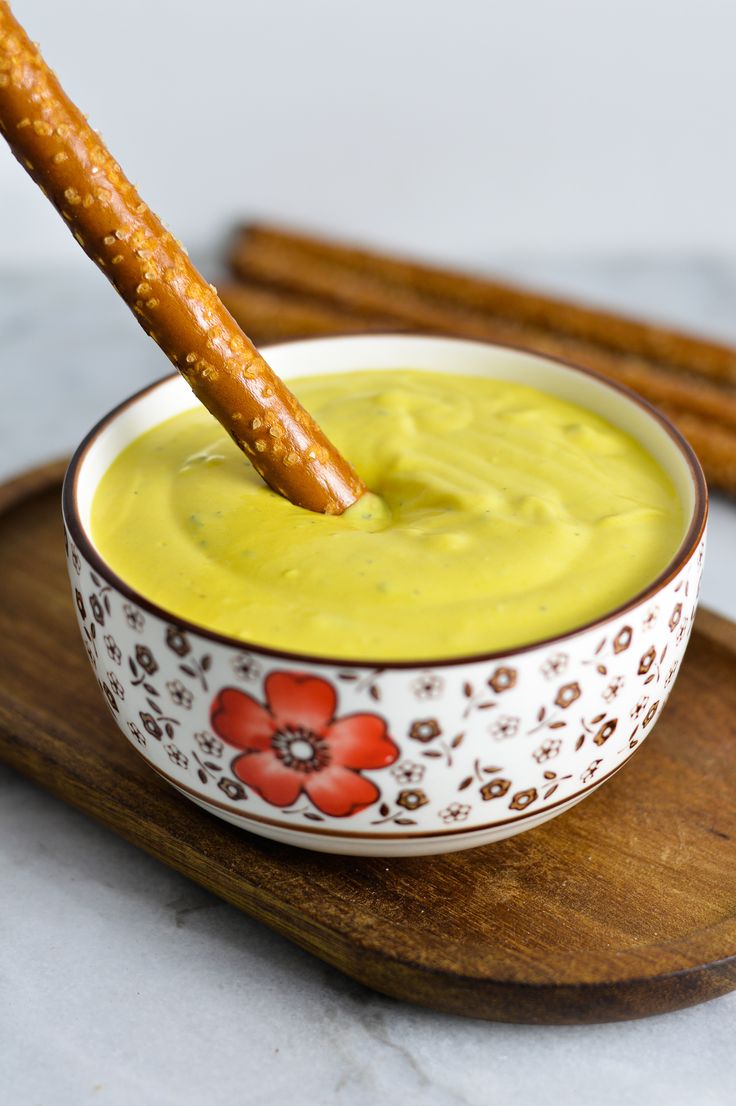 a small bowl filled with yellow sauce and a pretzel sticking out of it