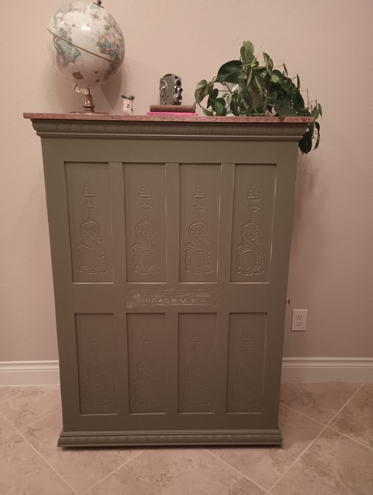 a green cabinet sitting on top of a tiled floor next to a potted plant