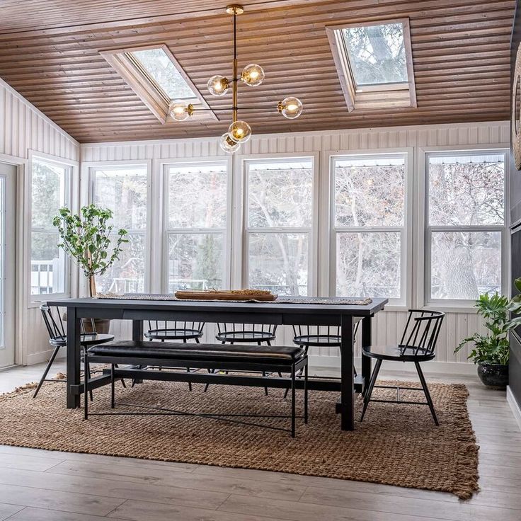 a dining room table with four chairs and a bench in front of the large windows