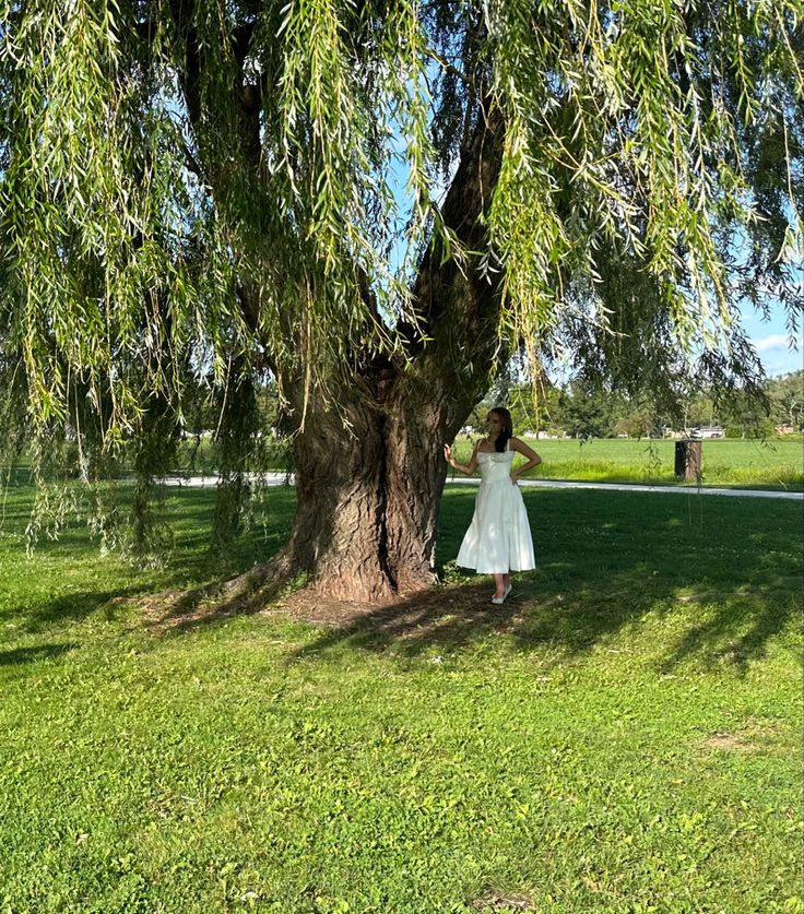 a woman in a white dress standing under a tree