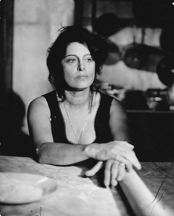 an old black and white photo of a woman sitting at a table with rolling dough