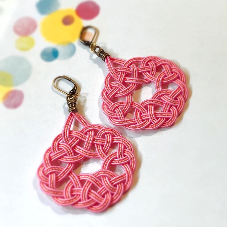 two pink earrings are on a white surface with polka dots and circles in the background