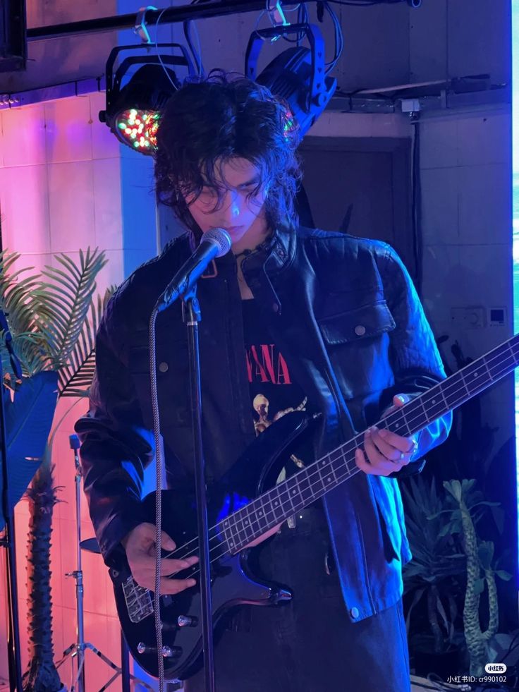 a young man is playing the bass guitar in front of a microphone and some plants