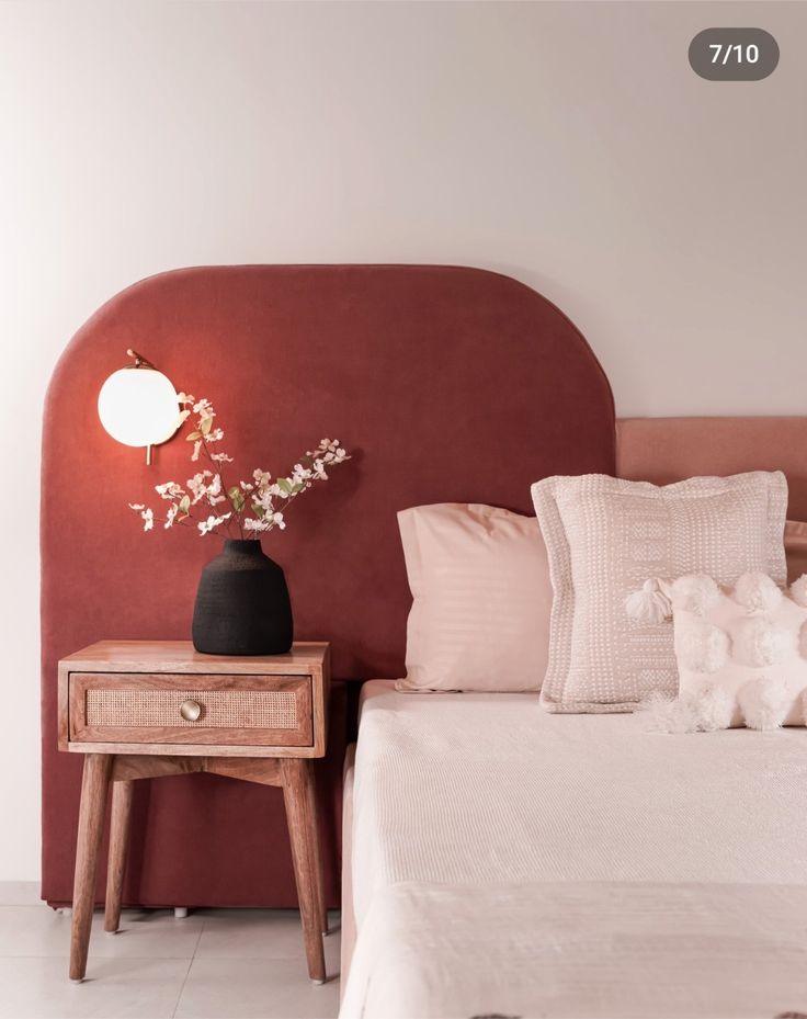 a bedroom with a red headboard and white bedding, flowers on the nightstand