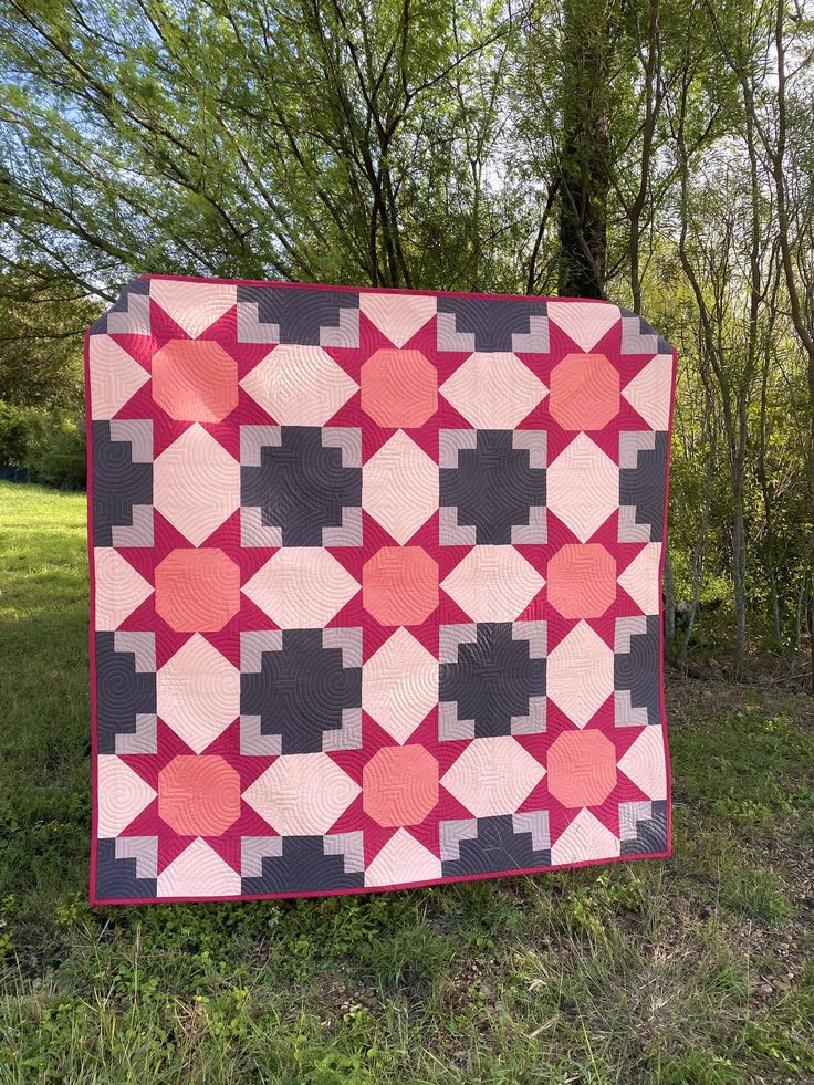 a pink and black quilt sitting in the grass