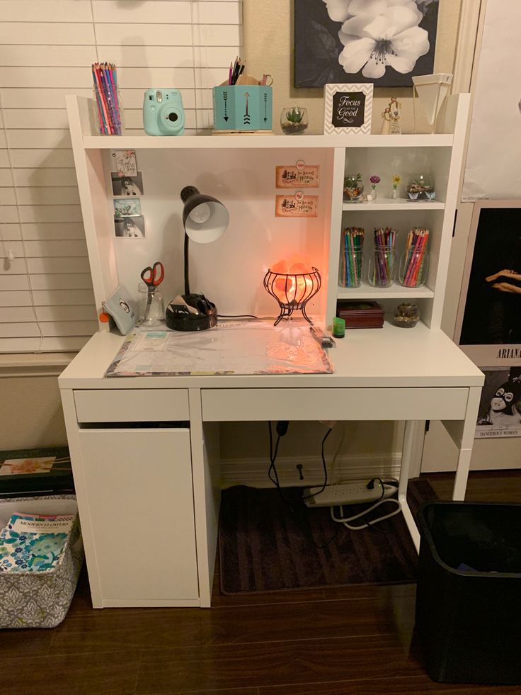 a white desk topped with a lamp next to a book shelf