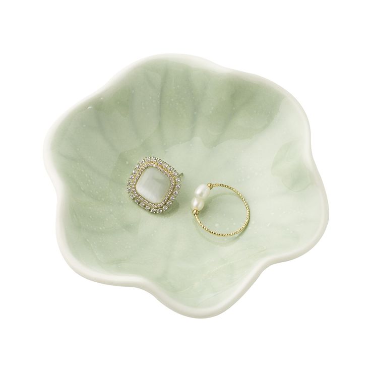 two rings sitting on top of a green flower shaped bowl with a pearl in the middle