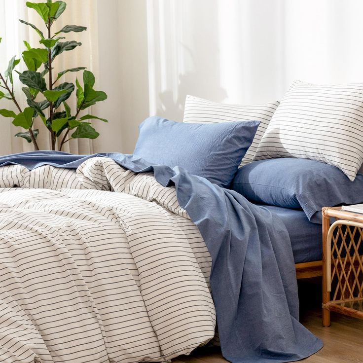 a bed with blue and white striped comforter next to a potted plant on a side table