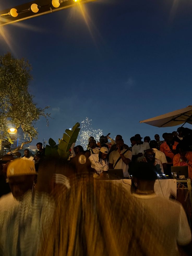 a large group of people sitting under umbrellas at an outdoor event with fireworks in the sky