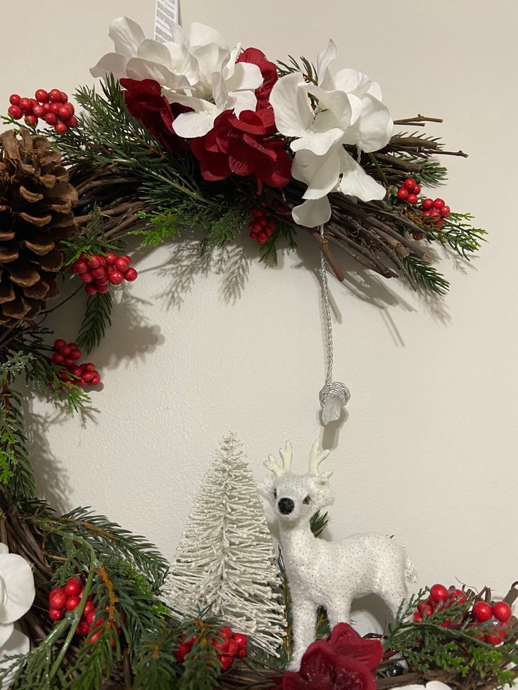 a christmas wreath decorated with white flowers and red berries, pine cones and deer figurines