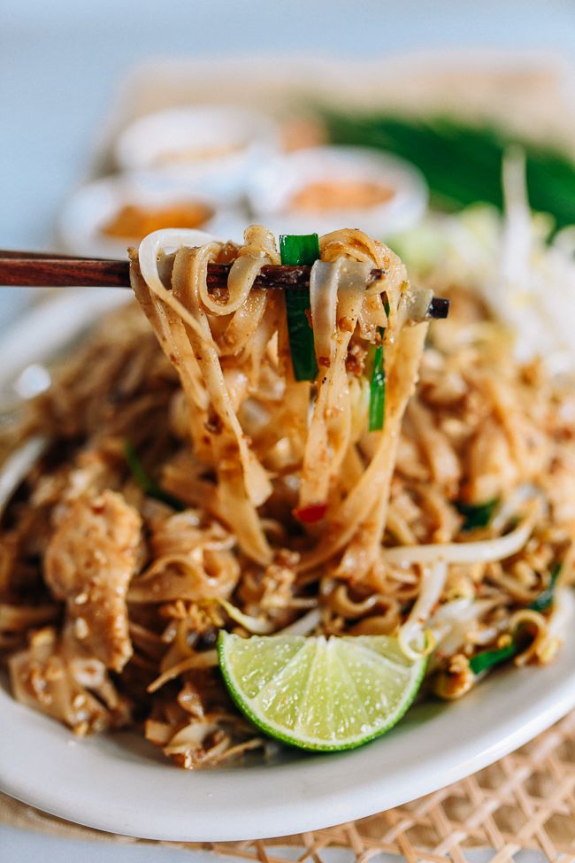 a white plate topped with noodles and meat next to chopsticks on a table