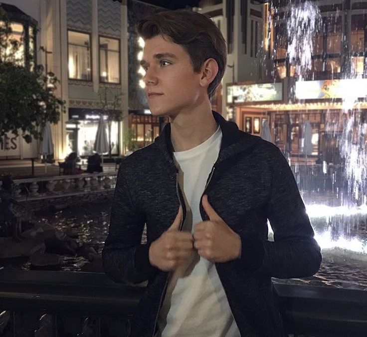 a young man standing in front of a fountain giving the thumbs up sign with both hands