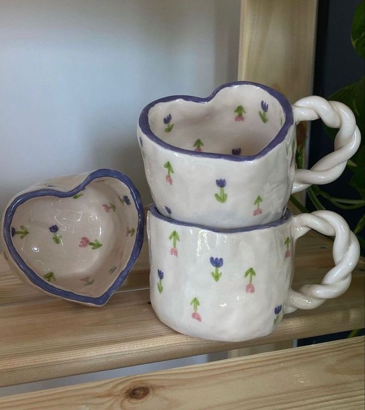 three coffee mugs sitting next to each other on a wooden shelf in front of a potted plant