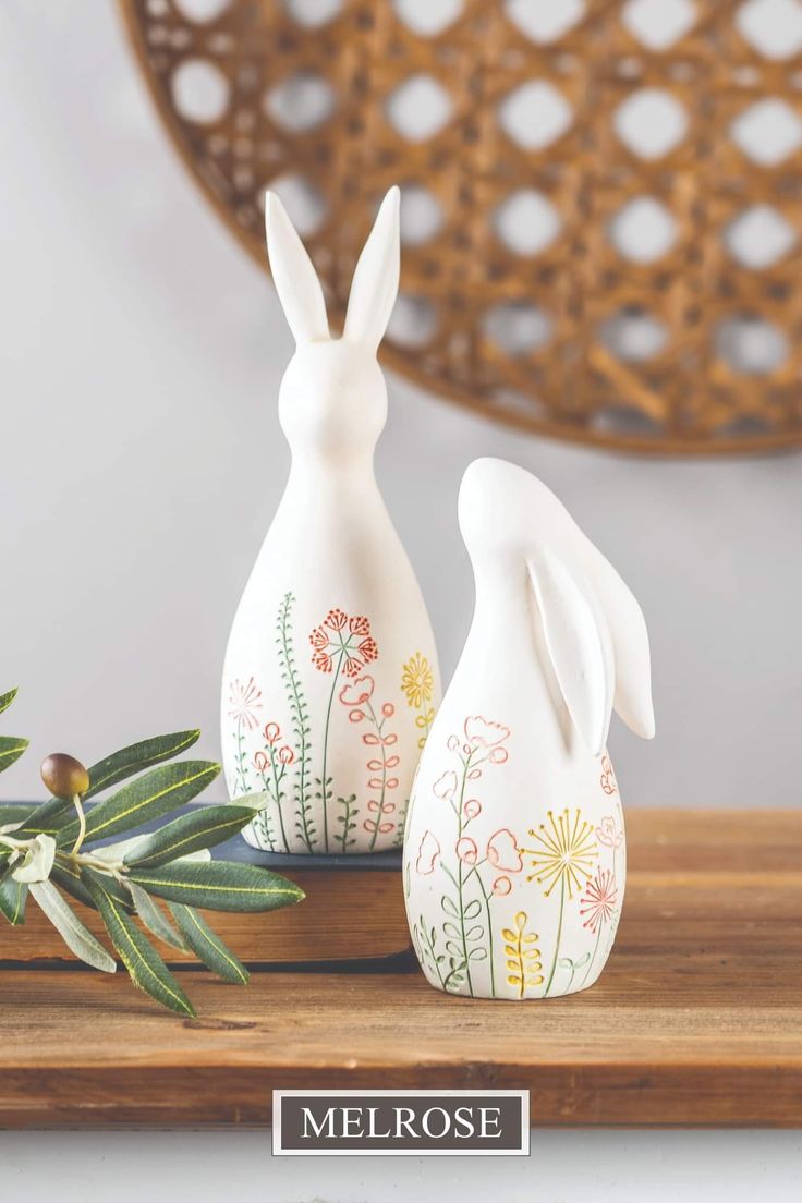 two white ceramic rabbits sitting on top of a wooden table